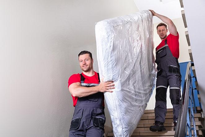 two workers hauling a box spring out of a building in Bay City MI